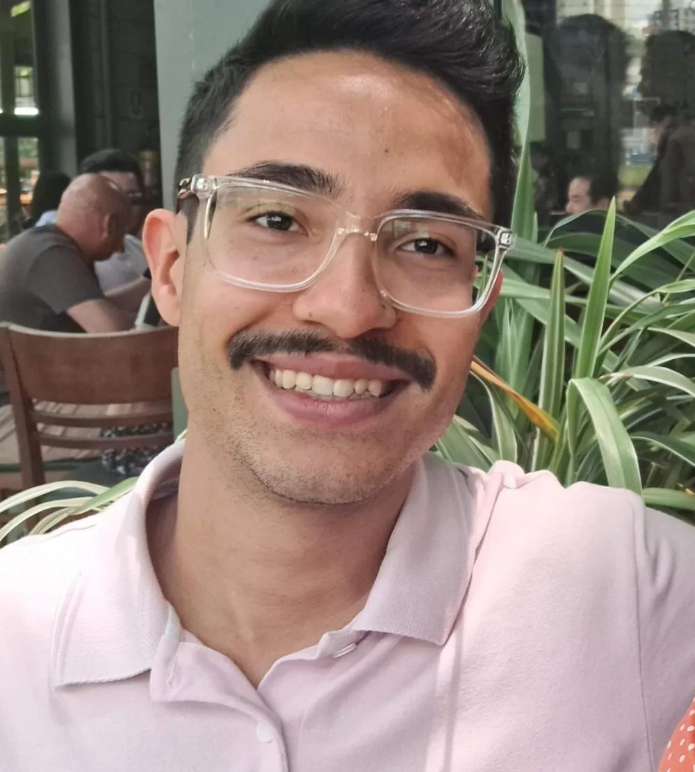 Andrey sorrindo em um café, com prédios de São Paulo refletidos ao fundo